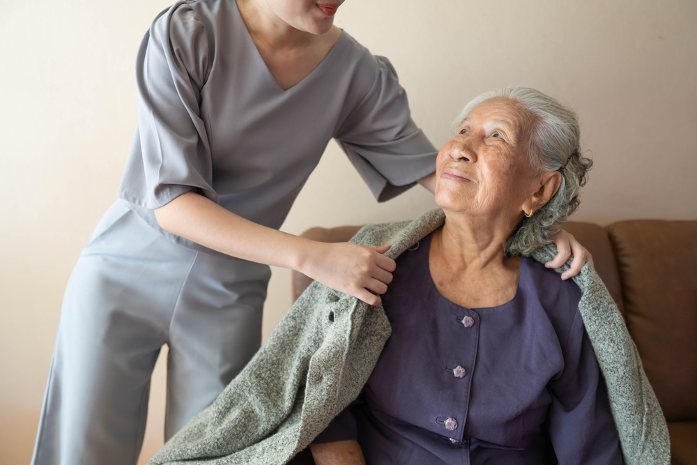 Elderly woman smiling while a nurse provides compassionate palliative care support at home