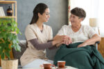 Senior man with Parkinson’s disease doing guided stretching exercises at home with caregiver assistance