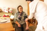 Licensed nurse providing skilled nursing care to an elderly patient at home, checking vital signs and reviewing medical treatment plan.